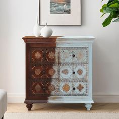 a white vase sitting on top of a wooden cabinet next to a painting in a living room