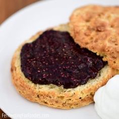 two biscuits with blueberry jam on them sit on a white plate next to a dollop of whipped cream