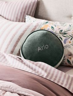 a bed with pink and white striped sheets, pillows and an oval pillow that says aro on it