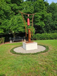 a sculpture in the middle of a grassy area with trees and bushes behind it,