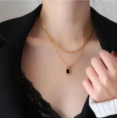 This necklace embodies a harmonious blend of textures and colors, with layers of lustrous gold stainless steel chains that elegantly cascade and culminate in a striking bezel-set black or white stone pendant. The contrast between the radiant gold and the deep black stone exudes a sense of intrigue and luxury, making it an ideal accessory for elevating any ensemble. With its versatile design and meticulous craftsmanship, this necklace becomes a symbol of refined elegance and modern style.Stainles Black Metal Jewelry With Delicate Chain, Modern Black Formal Chain Necklace, Elegant Black Gold Plated Chain Necklace, Elegant Black Gold-plated Chain Necklace, Black Delicate Chain Metal Necklace, Modern Black Chain Necklace For Formal Occasions, Luxury Black Chain Necklace As A Gift, Luxury Black Metal Necklace, Everyday Black Jewelry With Gold Chain