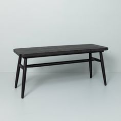 a wooden table with black legs on a white background in front of a gray wall