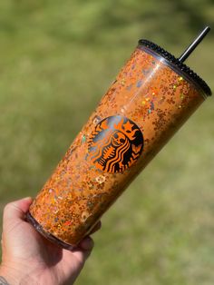 a hand holding a starbucks cup with orange sprinkles and a black lid