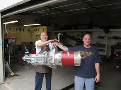 two men standing next to each other in front of a large engine on a machine