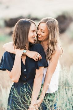 two women hugging each other while standing in tall grass with their arms around each other