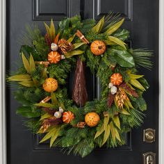 a wreath with oranges, pine cones and leaves is hanging on the front door