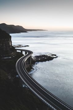 an aerial view of a highway going over the ocean with mountains in the back ground