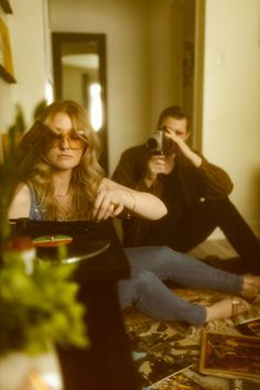 a man and woman sitting on the floor in front of a record player holding a camera