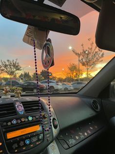 the sun is setting over a parking lot with cars parked in it and there are beads hanging from the dash board