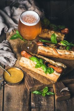 two hotdogs and a glass of beer on a wooden table next to some bread