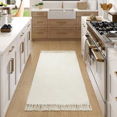 a kitchen with white cabinets and wooden floors is shown in this image, the rug on the floor has fringes hanging from it