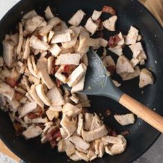 chicken and bacon cooking in a skillet with a wooden spoon