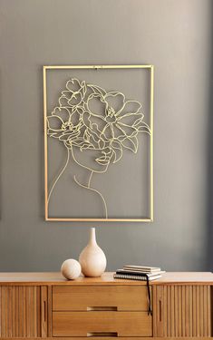 a white vase sitting on top of a wooden dresser next to a wall mounted art piece