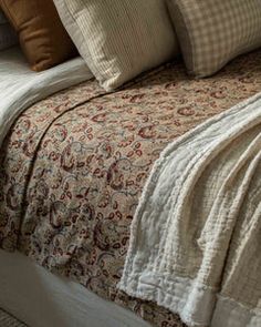 a bed with several pillows on top of it next to a night stand and lamp