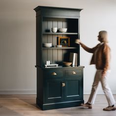 a man walking past a black bookcase with bowls and plates on top of it