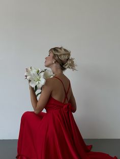 a woman in a red dress sitting on the floor with flowers behind her back to the camera