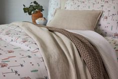 a bed covered in white and brown sheets with a potted plant next to it