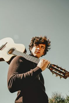 a man holding an acoustic guitar in his right hand and looking up at the sky