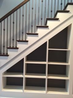 an open bookcase under the stairs in a room with white walls and black railings