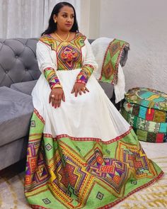 a woman is sitting on a couch wearing a colorful dress and matching jewelry with her hands in her pockets