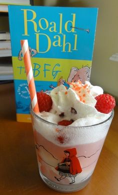 a book is on the table next to a glass with ice cream and raspberries