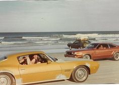 two cars driving on the beach with people in the back seat and one car behind them