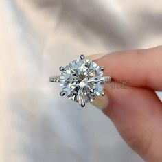 a woman's hand holding an engagement ring with a diamond in the center, on top of her finger