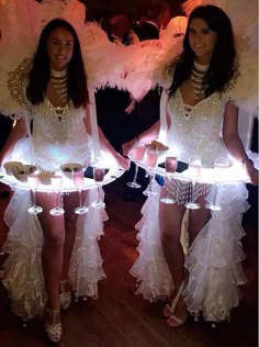 two women in white dresses holding trays with cupcakes on them