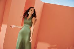 a woman in a green dress standing against an orange wall with her hand on her hip