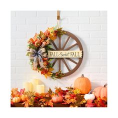 a wreath with fall leaves and pumpkins is hanging on the wall next to candles