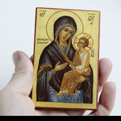 a hand holding a small wooden icon with an image of the virgin mary and child jesus