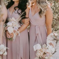 three bridesmaids in dusty pink dresses standing together with their bouquets and flowers