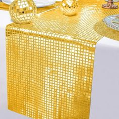 a table topped with a yellow cloth and two shiny disco ball decorations on top of it