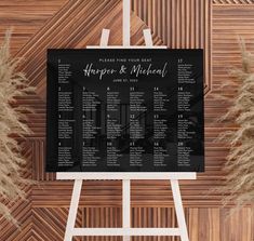 a black and white wedding seating plan on a easel next to pamy grass