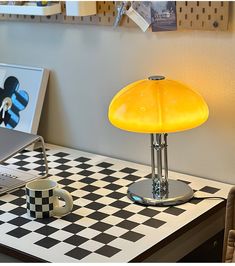 a yellow lamp sitting on top of a desk next to a laptop computer and coffee cup