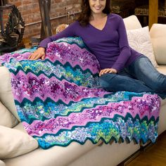 a woman sitting on a couch with a crocheted blanket