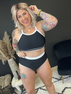 a woman in a black and white swimsuit posing for the camera with tattoos on her arms