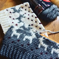 two knitted mitts sitting on top of a wooden table next to a ball of yarn