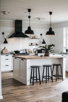 a kitchen with white cabinets and black pendant lights hanging from the ceiling over the island