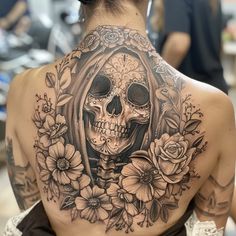 a woman's back with a skull and flowers tattoo on her upper half sleeve