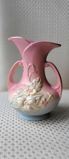 a pink and white vase sitting on top of a table next to a wallpaper