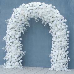 a white wedding arch with flowers on the side and blue wall behind it, in front of a wooden floor