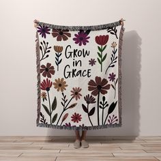 a woman standing in front of a white wall holding a blanket with flowers on it