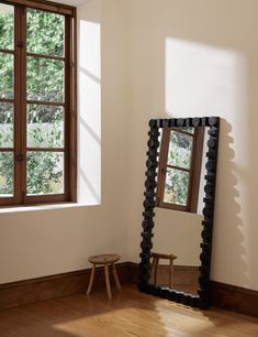 a mirror sitting on top of a hard wood floor next to a wooden stool and window