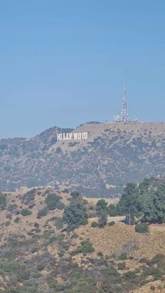 the hollywood sign on top of a hill with trees in the foreground and an oil rig in the background