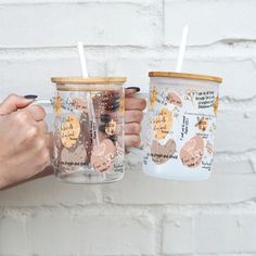 two people holding coffee mugs in front of a brick wall with writing on them