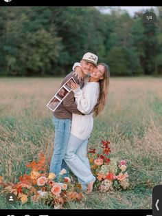 two people are hugging in the middle of a field with flowers and trees behind them