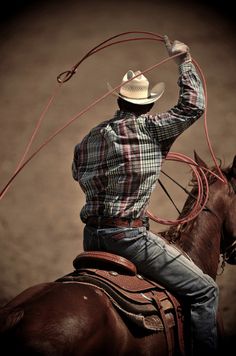 a man riding on the back of a brown horse wearing a cowboy hat and lasso