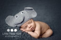 a baby wearing a knitted elephant hat laying on top of a blanket with its eyes closed