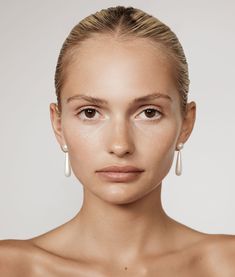 a woman with white makeup and earrings on her head, looking at the camera while she is